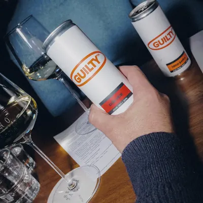 A hand holding a Cola Vice can at the table at Tintino, wine and menu in frame.