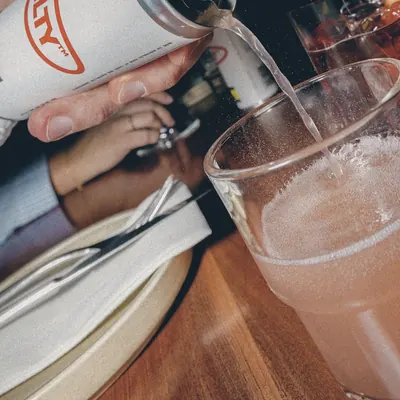 A GUILTY can being poured into a glass at the table at Tintino, spritz and place setting in frame.